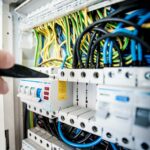 Hand of electrician working on a circuit breaker panel with colorful wires, ensuring safe electrical connections.