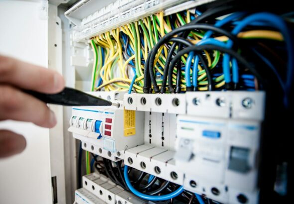 Hand of electrician working on a circuit breaker panel with colorful wires, ensuring safe electrical connections.